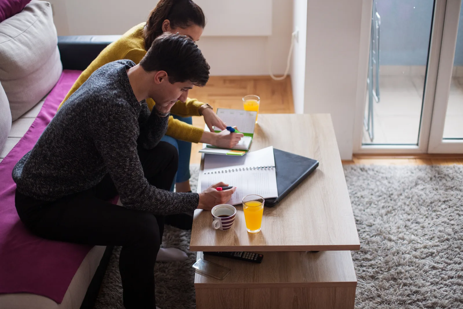 A couple comparing options together at their living room table, with a notebook, calendar, and mugs of coffee.