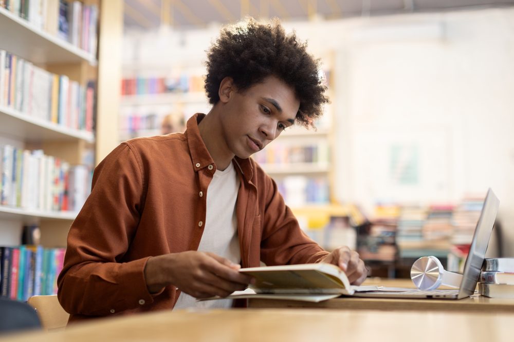 University student at a library desk with flashcards and an open laptop
