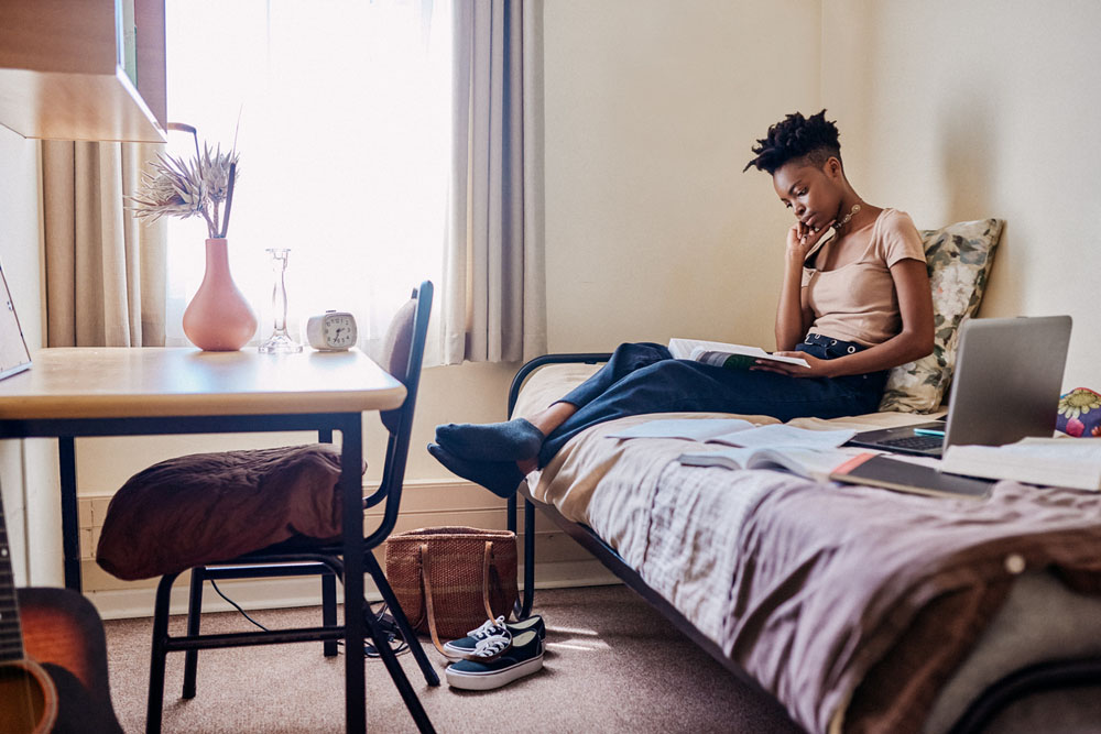 A young adult with ADHD studying in a dorm room while managing independent living responsibilities like bills, chores, and routines for a balanced student life.