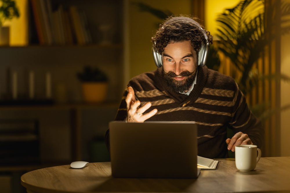 Woman on a video call at a kitchen table at night, mug beside the laptop