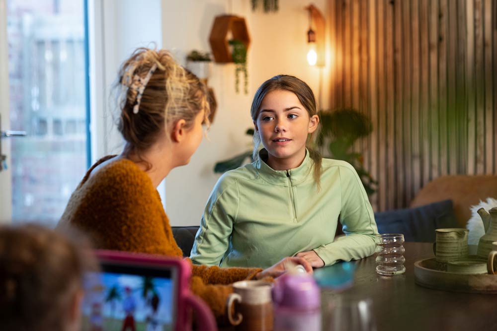 A teenage girl talks with her mother at the kitchen table, illustrating how open conversations and guidance help teens with ADHD manage impulsive behaviours more effectively.