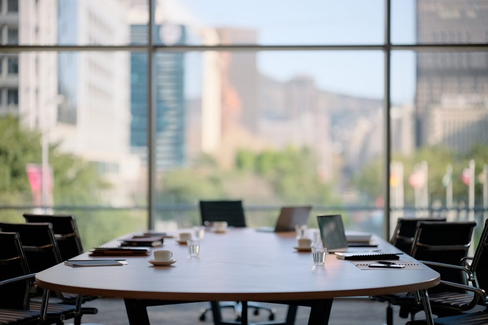 Four colleagues around a boardroom table with one person writing in a notebook