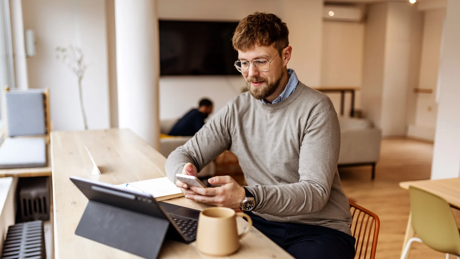 Man at a bright home office desk checking the calendar on his phone to rebook an appointment.
