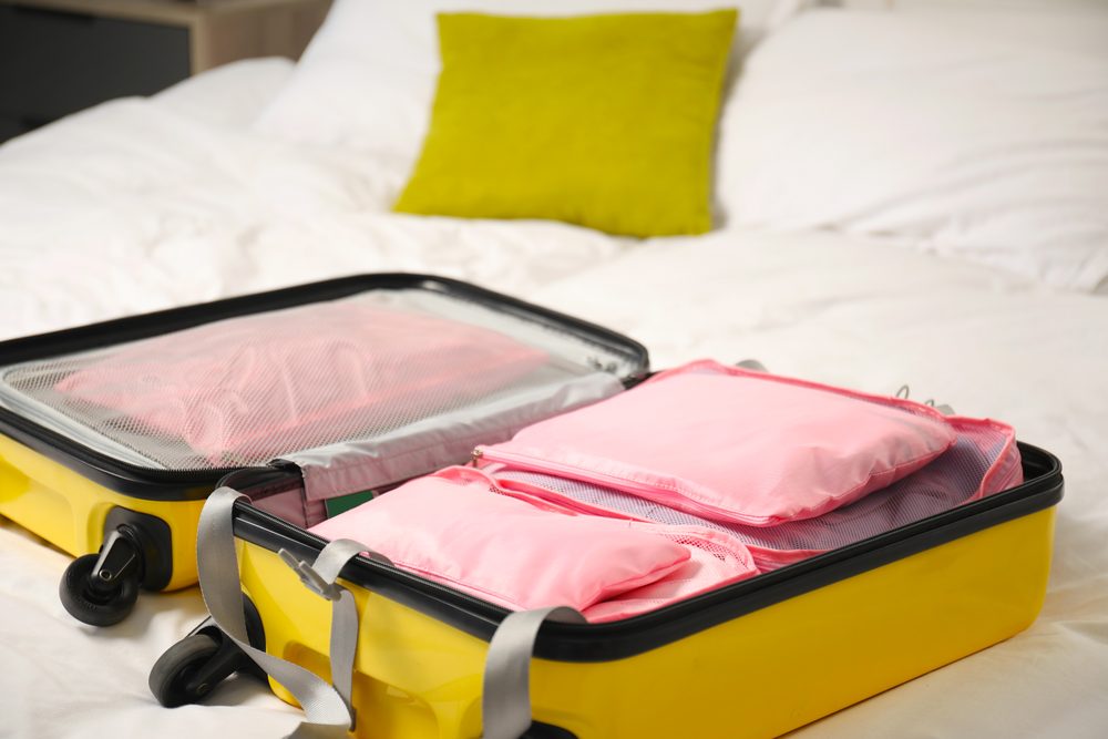 Open suitcase on a bed with folded clothes, a phone charger and a passport laid out