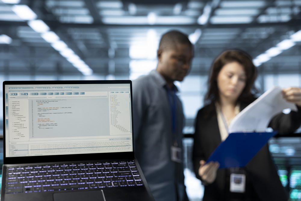 Employee reading a printed document at a desk with a laptop and a cup of coffee