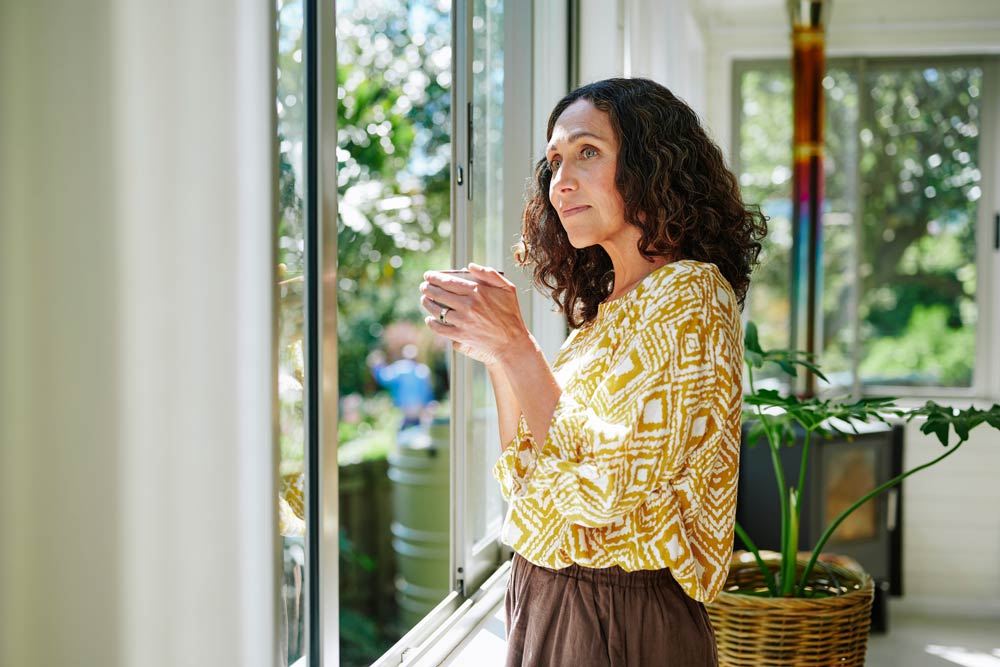 A woman stands by a window holding a cup, reflecting quietly, symbolizing the unique and often hidden presentation of ADHD in women.