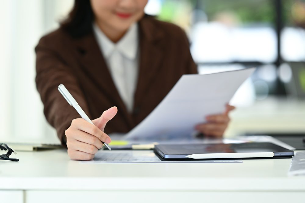 Woman in her fifties at a dining table with a laptop, pill organiser and school forms