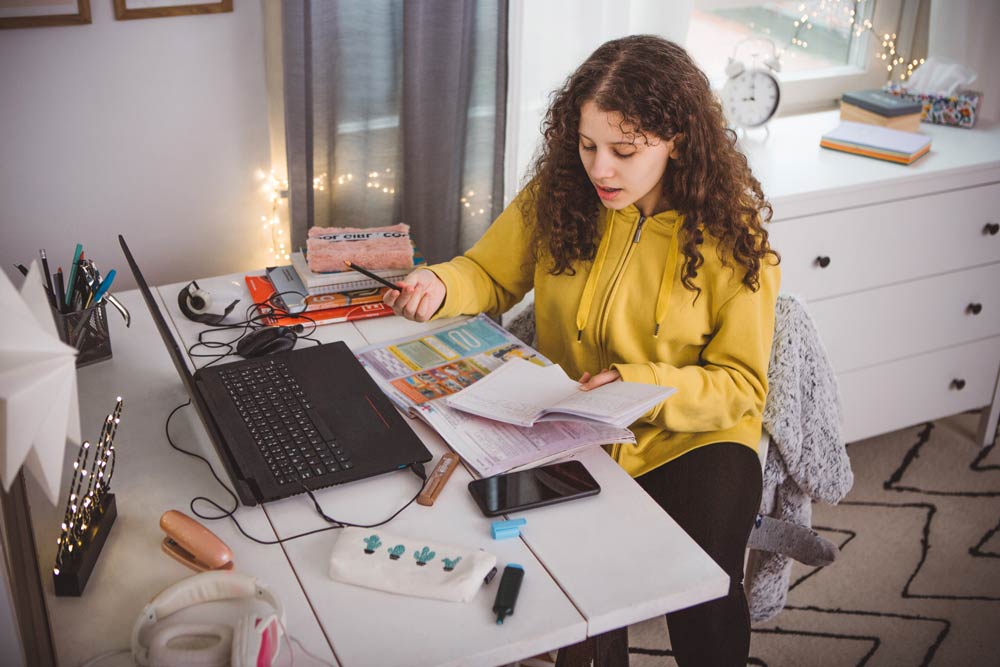 A teenage girl studies at her desk with a laptop and open books, showing how structured planning helps teens with ADHD set academic and career goals.