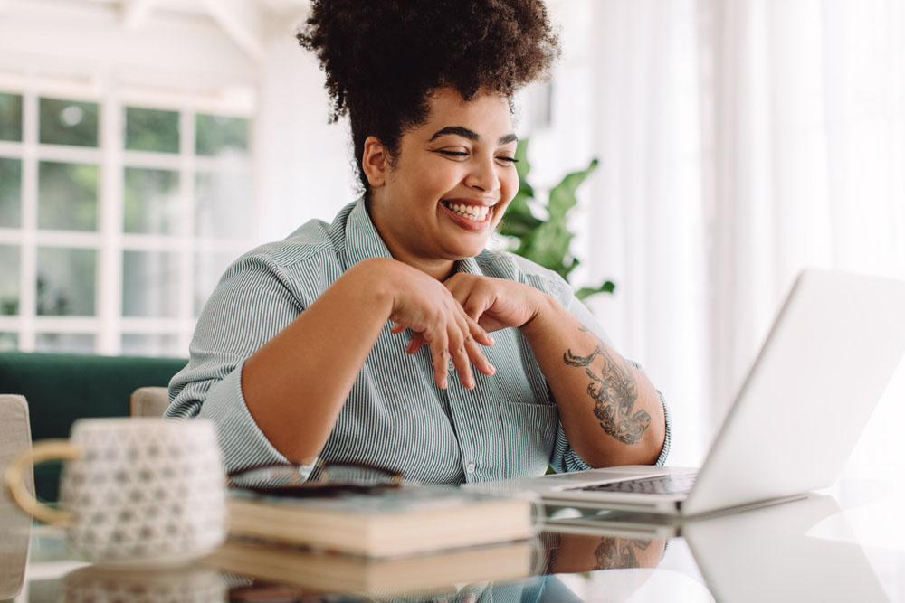A smiling student with ADHD working on a laptop at home, representing the importance of setting healthy boundaries at school and work to prevent burnout and support well-being.