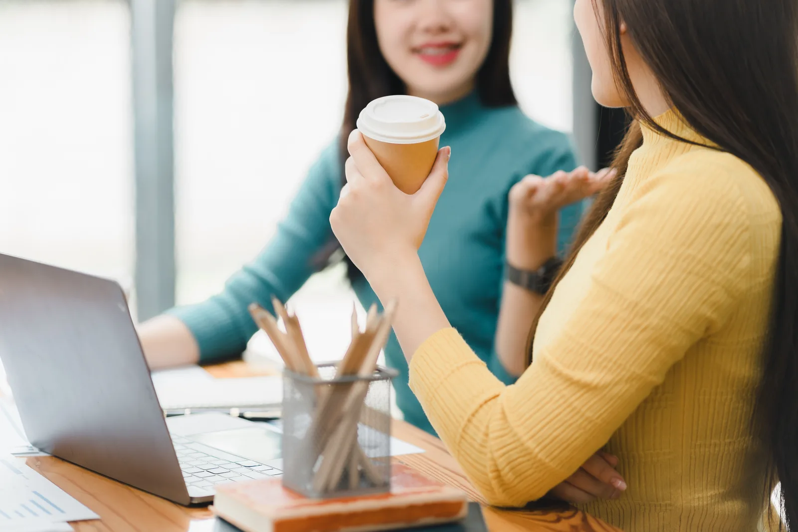 Two colleagues having a thoughtful one-on-one conversation over coffee in an office lounge, reflecting the personal decision of disclosing ADHD at work.