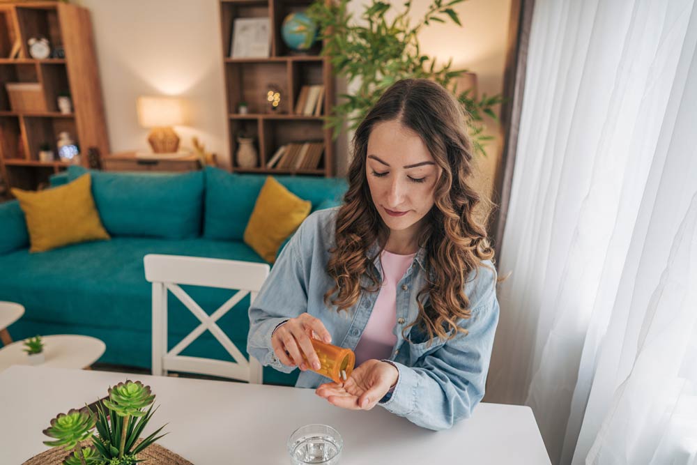 Woman sitting at a table taking ADHD medication with a glass of water, representing stimulant treatment for focus and attention.