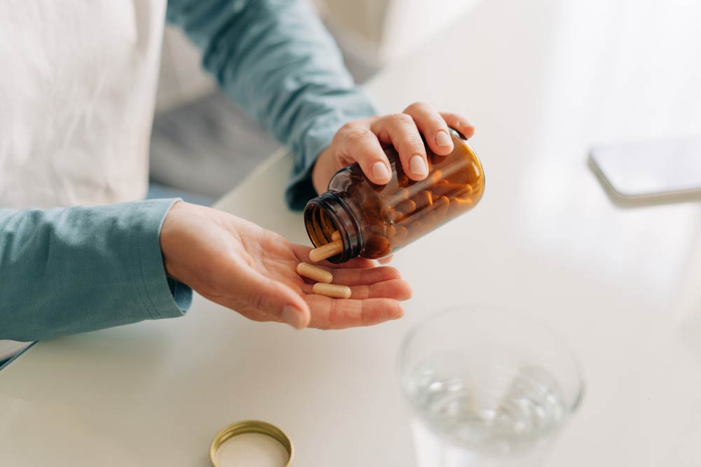 Close-up of a person pouring supplement capsules from a brown bottle into their hand, representing natural remedies and alternative treatments for ADHD.