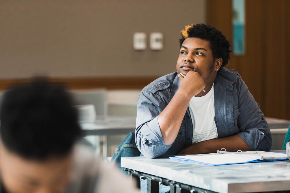 Teen student sitting at a desk and looking thoughtful, representing self-identity and self-esteem challenges in ADHD.
