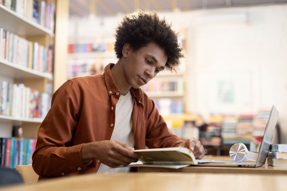 Young man studying in a library, representing the evolution of ADHD understanding through education and research.