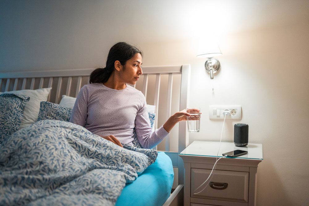 A woman sitting in bed holding a glass of water, representing the importance of establishing calming bedtime routines for better sleep with ADHD.