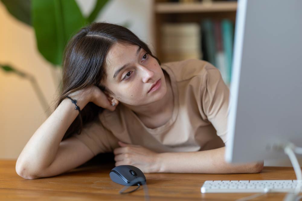 Young girl leaning on a desk and staring at a computer screen, illustrating the challenges of focus and attention linked to inattentive ADHD.