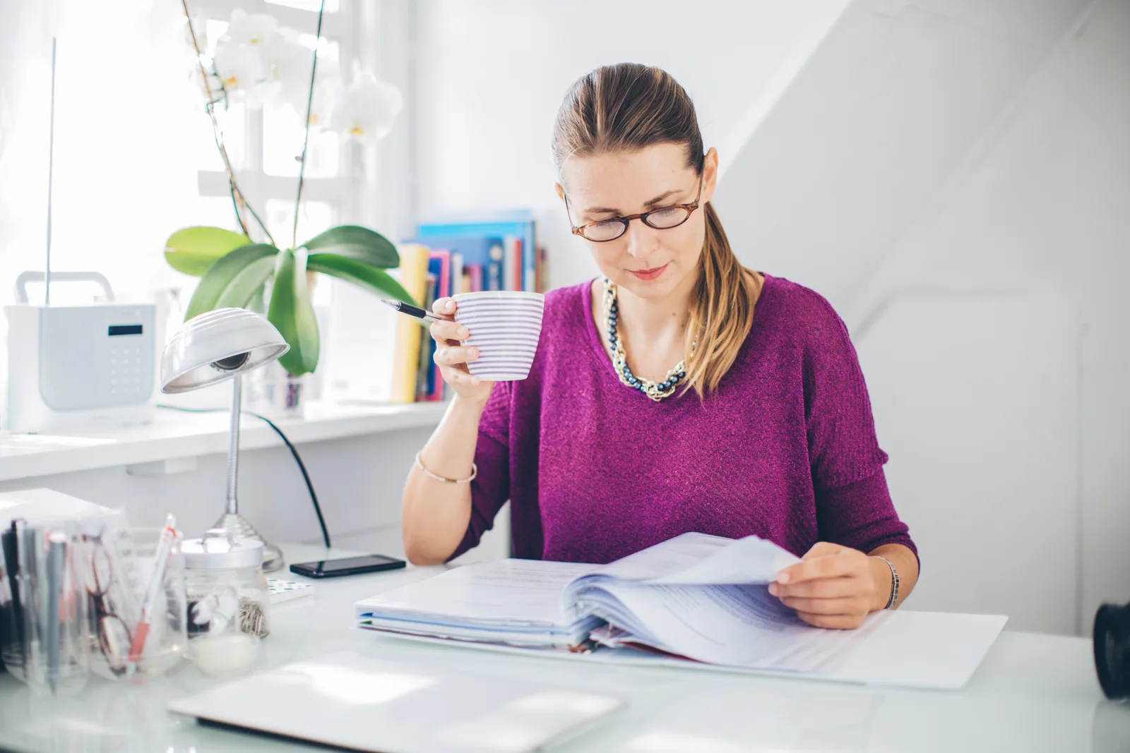 Woman at a bright home desk carefully reading through a detailed document, understanding what her ADHD assessment fee covers.