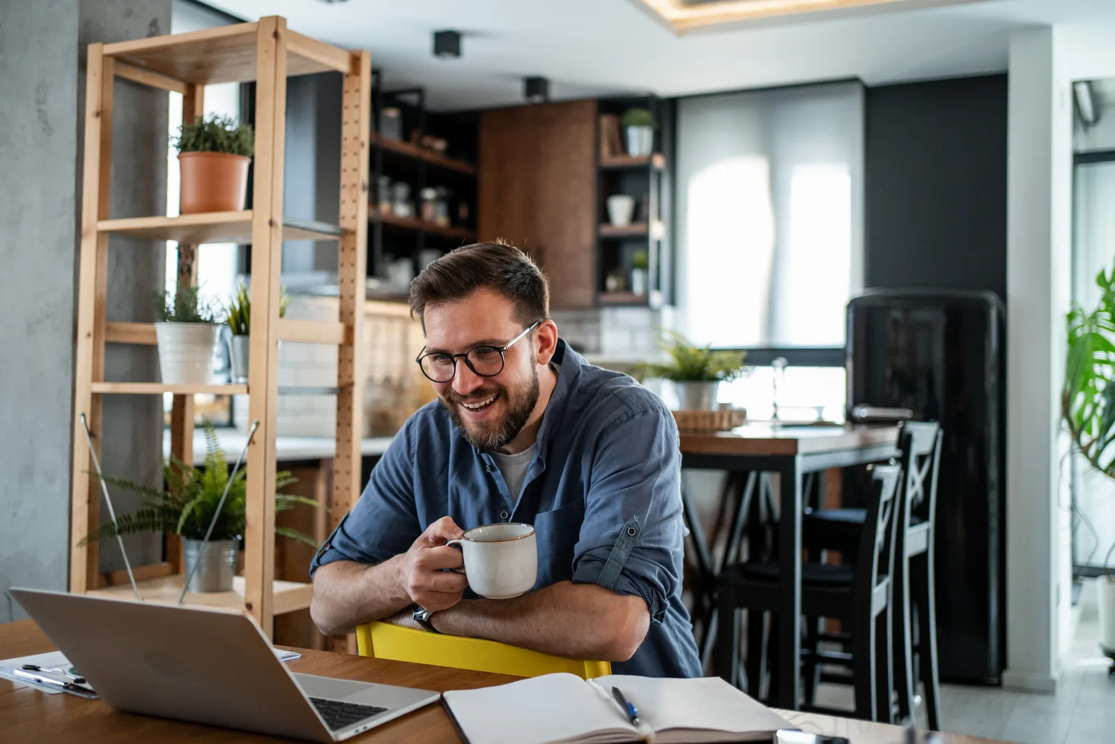 A man speaks with a clinician over a video call on his laptop at a bright kitchen table, taking part in a virtual ADHD assessment from home.