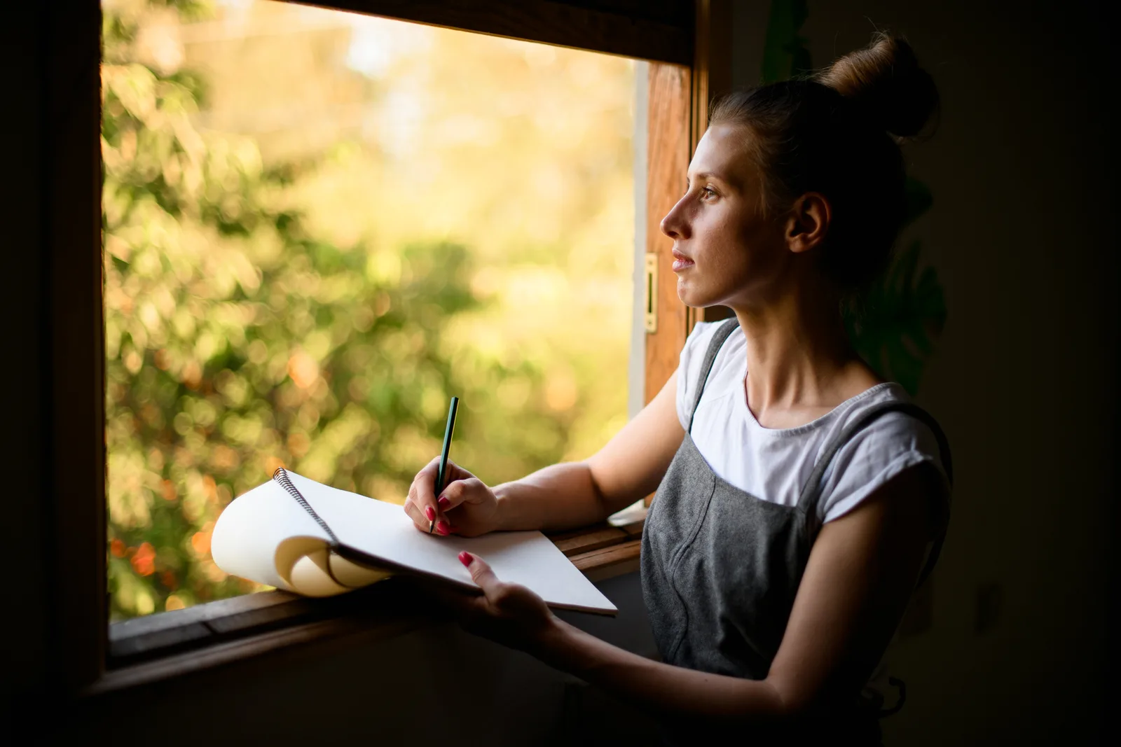 A young woman sitting by a window with a journal and a cup of tea, reflecting on the results of her ADHD assessment.