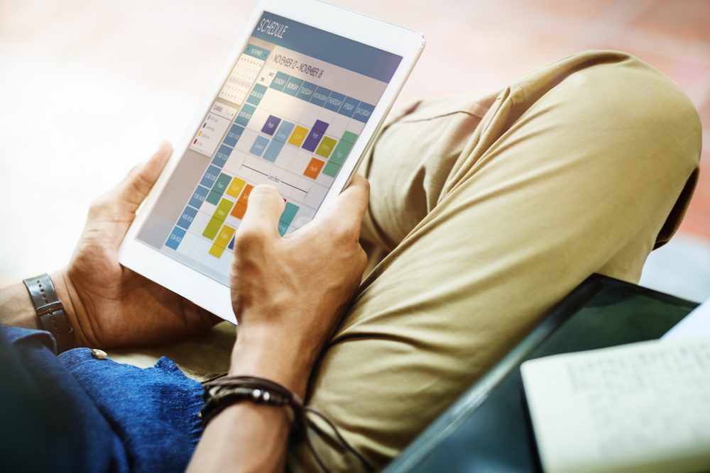 Woman at a kitchen table comparing a tablet planner with the calendar on her phone