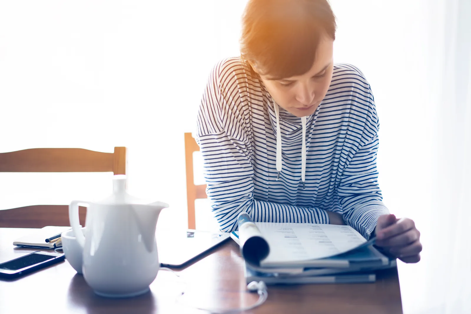 A woman reading a printed report at her kitchen table with a cup of coffee, reviewing the results of her ADHD assessment.