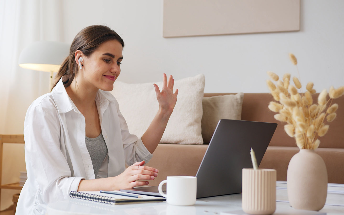 Woman waving during a virtual ADHD consultation call, sitting on a couch with a laptop