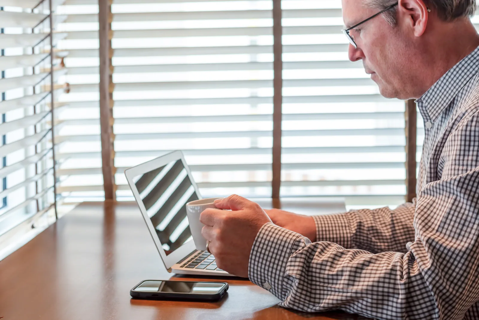 A man at his kitchen island in Alberta prepares for an online ADHD assessment on his laptop over morning coffee