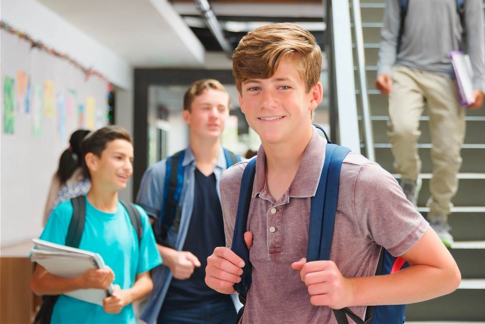 A teenage student with a backpack smiling in a busy high school hallway, representing strategies for teens with ADHD to manage organization, time, and school success.